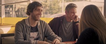 Movie still from “The Final Girls” (2015), directed by Todd Strauss-Schulson – Two men sitting at a table and smiling; Medium shot, Over the shoulder angle