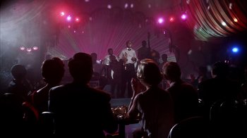 Movie still from “The Five Pennies” (1959), directed by Melville Shavelson – A group of people sitting at a table in front of a microphone; Wide shot, Over the shoulder angle