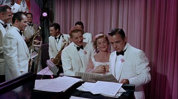 Movie still from “The Five Pennies” (1959), directed by Melville Shavelson – A man and a woman in a white suit and a man in a white suit and a woman in a white suit and a man in a white; Medium shot, Low angle