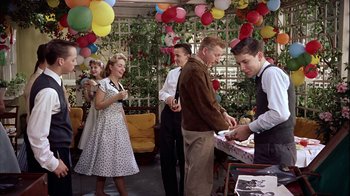 Movie still from “The Five Pennies” (1959), directed by Melville Shavelson – A group of people standing around a table with a cake on it; Medium shot, High angle
