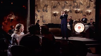 Movie still from “The Five Pennies” (1959), directed by Melville Shavelson – A man in a blue suit is on a stage with a microphone; Wide shot, Low angle