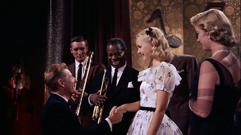 Movie still from “The Five Pennies” (1959), directed by Melville Shavelson – A man and a woman shaking hands in front of a band; Medium shot, Over the shoulder angle