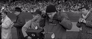 Movie still from “The Fortune Cookie” (1966), directed by Billy Wilder – Two men are standing next to each other in front of a crowd; Medium shot, Over the shoulder angle