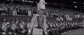 Movie still from “The Fortune Cookie” (1966), directed by Billy Wilder – A man in a marching band uniform walking in front of a crowd; Medium shot, High angle