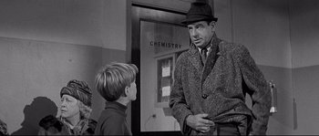 Movie still from “The Fortune Cookie” (1966), directed by Billy Wilder – An older man and a young boy in front of a chemistry sign; Medium shot, Over the shoulder angle