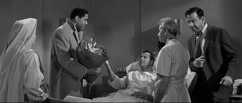 Movie still from “The Fortune Cookie” (1966), directed by Billy Wilder – A man holding a bouquet of flowers in a hospital bed; Medium shot, Over the shoulder angle