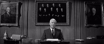 Movie still from “The Fortune Cookie” (1966), directed by Billy Wilder – An older man sitting at a desk in front of a painting; Medium shot, Over the shoulder angle
