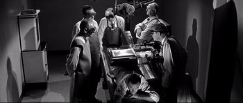 Movie still from “The Fortune Cookie” (1966), directed by Billy Wilder – A black and white photo of a group of men working on a machine; Medium shot, High angle