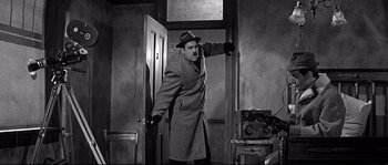 Movie still from “The Fortune Cookie” (1966), directed by Billy Wilder – A man wearing a coat and a hat standing in front of an open door; Medium shot, Low angle