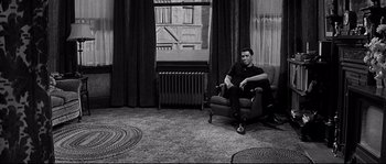 Movie still from “The Fortune Cookie” (1966), directed by Billy Wilder – A man sitting on a chair in a room; Wide shot, High angle