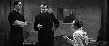 Movie still from “The Fortune Cookie” (1966), directed by Billy Wilder – A man smoking a cigarette while another man watches; Medium shot, Over the shoulder angle