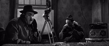 Movie still from “The Fortune Cookie” (1966), directed by Billy Wilder – Two men sitting in front of a camera; Medium shot, Over the shoulder angle