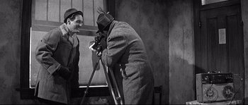 Movie still from “The Fortune Cookie” (1966), directed by Billy Wilder – An older man is taking a picture of another man; Medium shot, Over the shoulder angle