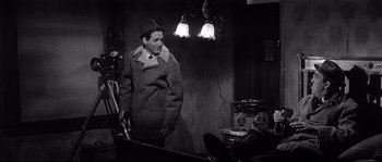 Movie still from “The Fortune Cookie” (1966), directed by Billy Wilder – A man standing in front of a lamp in a dimly - lit room; Medium shot, Over the shoulder angle