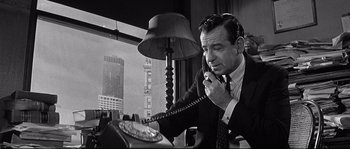 Movie still from “The Fortune Cookie” (1966), directed by Billy Wilder – A man talking on a phone while sitting at a desk; Medium shot, High angle