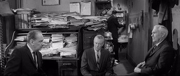 Movie still from “The Fortune Cookie” (1966), directed by Billy Wilder – An older man sitting in front of stacks of papers; Medium shot, High angle