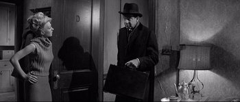 Movie still from “The Fortune Cookie” (1966), directed by Billy Wilder – A black and white photo of a man in a suit and hat holding a briefcase; Medium shot, Over the shoulder angle