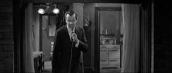 Movie still from “The Fortune Cookie” (1966), directed by Billy Wilder – A black and white photo of a man holding a microphone; Medium shot, Over the shoulder angle