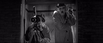Movie still from “The Fortune Cookie” (1966), directed by Billy Wilder – A man in a hat and a man in a trench coat with a camera; Medium shot, Low angle
