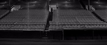 Movie still from “The Fortune Cookie” (1966), directed by Billy Wilder – A man standing in a stadium with rows of seats; Extreme Wide shot, High angle