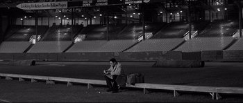Movie still from “The Fortune Cookie” (1966), directed by Billy Wilder – A man sitting on top of a bench next to a bag; Wide shot, High angle