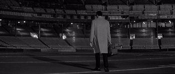 Movie still from “The Fortune Cookie” (1966), directed by Billy Wilder – A man in a long coat is standing in a stadium; Wide shot, High angle