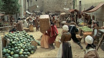 Movie still from “The Four Musketeers: Milady's Revenge” (1974), directed by Richard Lester – A group of people walking through a market area; Wide shot, High angle