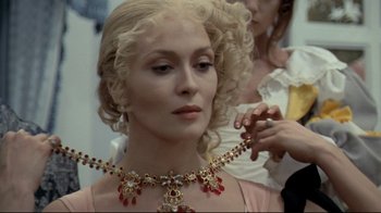 Movie still from “The Four Musketeers: Milady's Revenge” (1974), directed by Richard Lester – A woman with blonde curly hair wearing a red necklace; Close Up shot, Over the shoulder angle