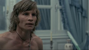 Movie still from “The Four Musketeers: Milady's Revenge” (1974), directed by Richard Lester – A man with long blonde hair wearing a cross necklace; Close Up shot, Over the shoulder angle