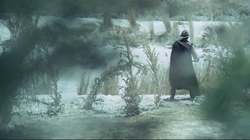 Movie still from “The Four Musketeers: Milady's Revenge” (1974), directed by Richard Lester – A man wearing a black cape walking in the snow; Wide shot, High angle