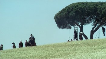 Movie still from “The Four Musketeers: Milady's Revenge” (1974), directed by Richard Lester – A group of people sitting under a tree on top of a hill; Extreme Wide shot, Low angle