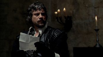 Movie still from “The Four Musketeers: Milady's Revenge” (1974), directed by Richard Lester – A man with a beard is holding a piece of paper in his hands; Medium shot, Over the shoulder angle