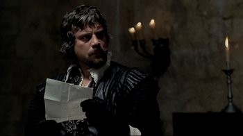 Movie still from “The Four Musketeers: Milady's Revenge” (1974), directed by Richard Lester – A man with a beard is holding a piece of paper in his hands; Medium shot, Over the shoulder angle