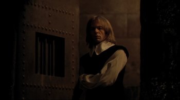 Movie still from “The Four Musketeers: Milady's Revenge” (1974), directed by Richard Lester – A man standing in front of a wall with bars; Medium shot, Over the shoulder angle