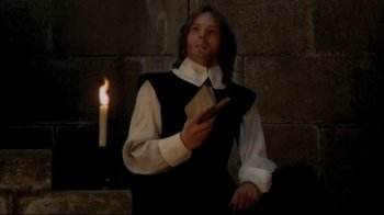 Movie still from “The Four Musketeers: Milady's Revenge” (1974), directed by Richard Lester – A man holding a book while standing next to a lit candle; Medium shot, Low angle