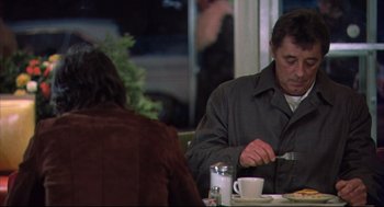 Movie still from “The Friends of Eddie Coyle” (1973), directed by Peter Yates – A man sitting at a table with a plate of food in front of him; Medium shot, Over the shoulder angle