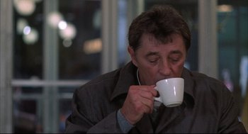 Movie still from “The Friends of Eddie Coyle” (1973), directed by Peter Yates – A man drinking a cup of coffee while wearing headphones; Close Up shot, Over the shoulder angle