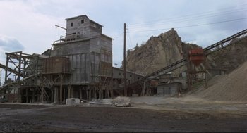 Movie still from “The Friends of Eddie Coyle” (1973), directed by Peter Yates – An old cement plant with a large rock in the background; Extreme Wide shot, High angle