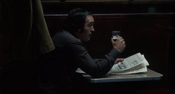 Movie still from “The Friends of Eddie Coyle” (1973), directed by Peter Yates – A man sitting at a table holding a glass of wine; Medium shot, Over the shoulder angle
