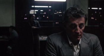 Movie still from “The Friends of Eddie Coyle” (1973), directed by Peter Yates – A man in a suit sitting in front of a window; Medium shot, Over the shoulder angle