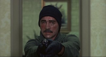 Movie still from “The Friends of Eddie Coyle” (1973), directed by Peter Yates – A man in a black hat is holding a gun in his hand; Close Up shot, Over the shoulder angle