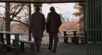 Movie still from “The Friends of Eddie Coyle” (1973), directed by Peter Yates – Two people are walking in a park near a bench; Wide shot, High angle