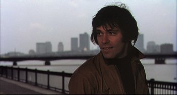 Movie still from “The Friends of Eddie Coyle” (1973), directed by Peter Yates – A man in a brown jacket standing in front of a body of water; Close Up shot, Low angle