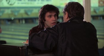 Movie still from “The Friends of Eddie Coyle” (1973), directed by Peter Yates – A man with long black hair is talking to another man in a black jacket; Close Up shot, Over the shoulder angle