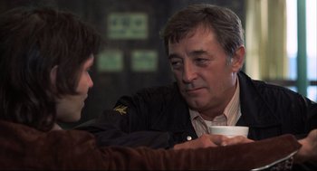 Movie still from “The Friends of Eddie Coyle” (1973), directed by Peter Yates – A man sitting next to another man holding a coffee cup; Close Up shot, Over the shoulder angle