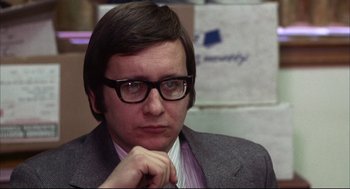 Movie still from “The Friends of Eddie Coyle” (1973), directed by Peter Yates – A man in a suit and glasses is looking at the camera; Close Up shot, Over the shoulder angle