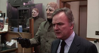 Movie still from “The Friends of Eddie Coyle” (1973), directed by Peter Yates – A wax statue of a man in a suit and tie next to another man in a suit and tie; Medium shot, Over the shoulder angle