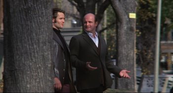 Movie still from “The Friends of Eddie Coyle” (1973), directed by Peter Yates – Two men standing next to each other near a tree; Medium shot, Low angle