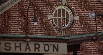 Movie still from “The Friends of Eddie Coyle” (1973), directed by Peter Yates – A man looking out of a window of a brick building; Wide shot, Low angle