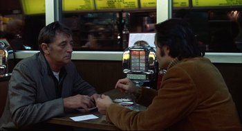 Movie still from “The Friends of Eddie Coyle” (1973), directed by Peter Yates – Two men sitting at a table in front of a machine; Medium shot, Over the shoulder angle